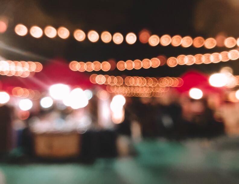 A blurry photo of a night market, strung with lights across the top.