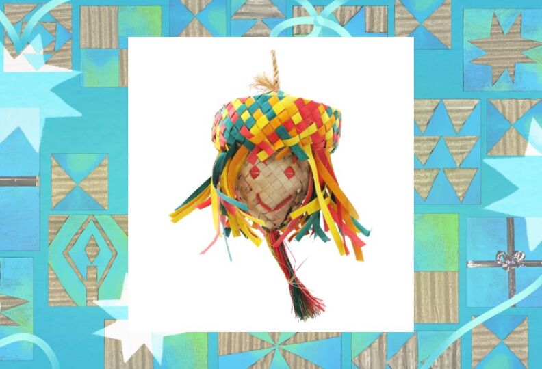 A photograph of a hanging bird toy made out of strips of natural materials that are woven together, to create an egg-shaped face that is wearing a wide-brimming hat and long strips of natural material hang down, like hair. The strips of the hat and hair are a variety of colors, including green, red, yellow and orange. The hat is wide enough and large enough to sprinkle seed inside, and provide a place for a lucky bird to perch and dine. The photo is set against decorative teal background accented with stars, holiday gift boxes and strands of ribbon.