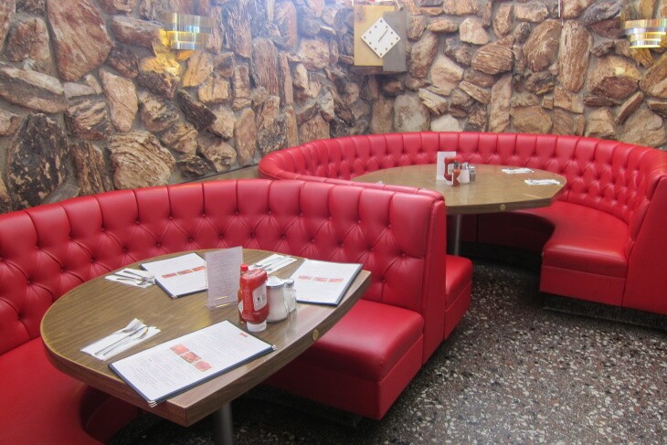Large circular booths are tufted in red vinyl with a lava rock wall behind them