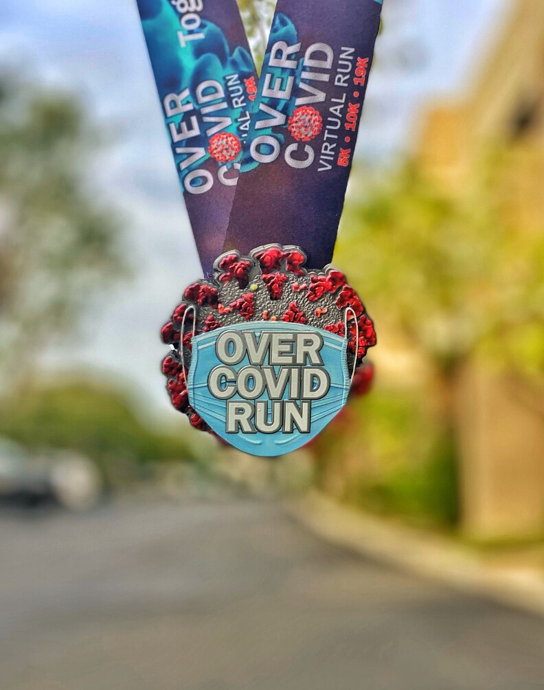 Photo of a medal on a blue ribbon. The medal is in the image of a Coronavirus molecule wearing a mask.