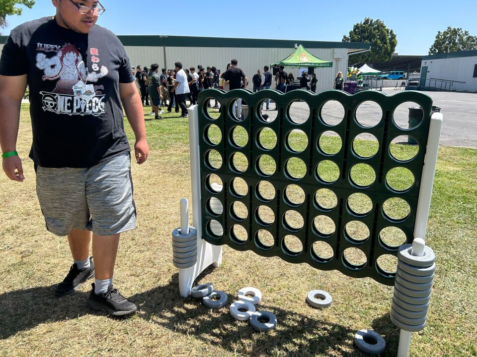 A male presenting person plays a Connect Four type game on a lawn