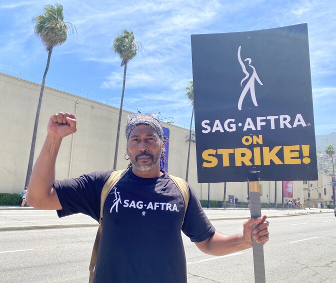  SAG-AFTRA member James Mathis III picketed outside of the Warner Bros. lot in Burbank on July 21, 2023. He wears a black SAG-AFTRA t-shirt and holds a sign that reads: "SAG-AFTRA on Strike!" 