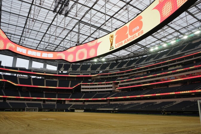 A brown field is surrounded by empty stadium seats and two soccer goals are placed at each end.