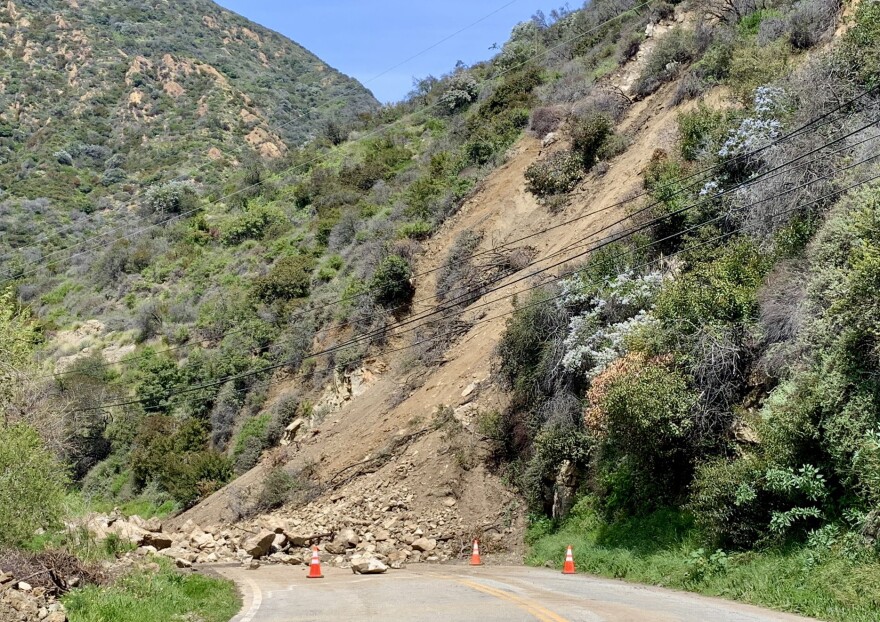 Rocks in the road off a hill covered with brush and green vegetation