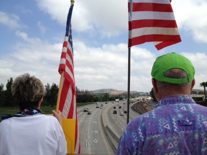 Protesters in Brea hold flags as they look down to traffic on the 57 freeway.