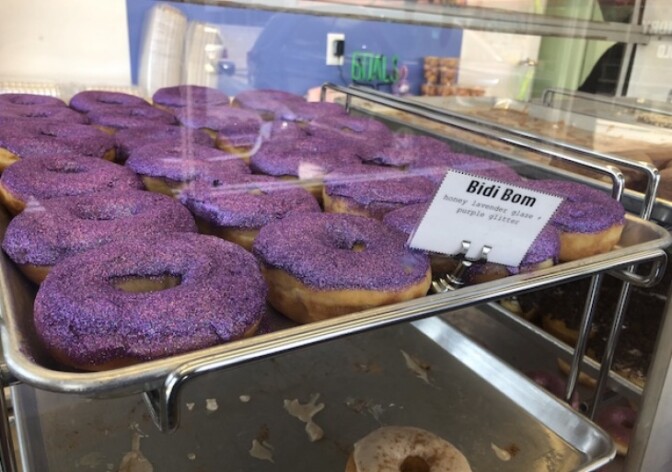 A tray of sparkly purple donuts sits inside a display case: These are the Bidi Bom, a tribute to the one and only Selena.