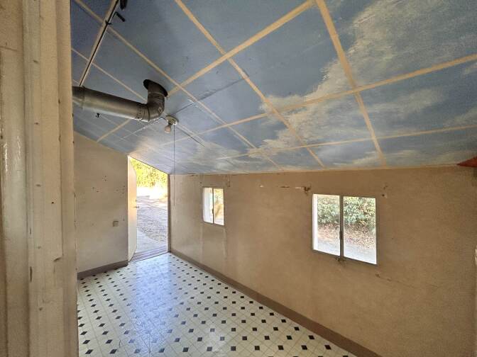 A small interior room with tan walls and two small windows. The ceiling is painted with a blue sky and clouds and is slopping downwards towards the windows.