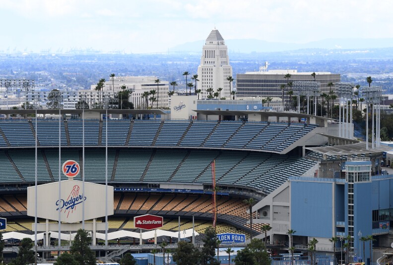 A Dodgers sign with the 76 logo on top is in the foreground with stadium seating and then, beyond, a view of L.A. City Hall