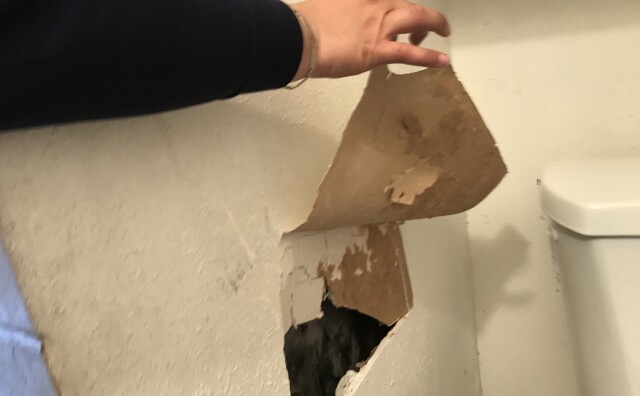 A woman points out for a large hole in the walls of her apartment.