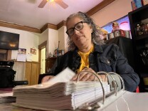 Cristina Campos sits at her family's kitchen table and flips through a binder of paperwork related to her apartment of 23 years.