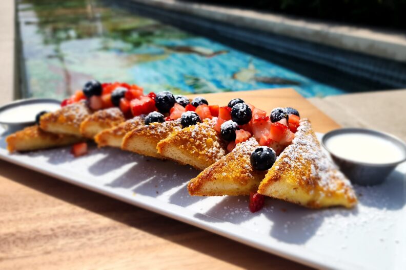 A plate of crispy French toast with chopped up berries and powdered sugar on top.