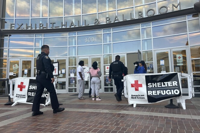 Police walk into a large building marked with banners that read "American Red Cross Shelter" 
