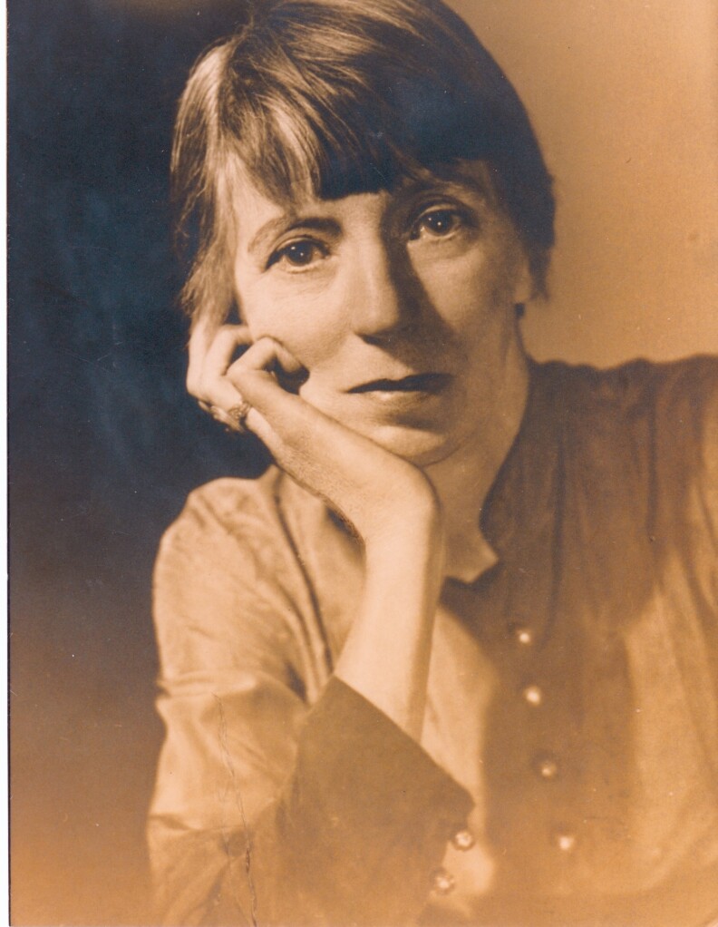 A sepia tone image of Margery Williams who poses with her hand on her chin.