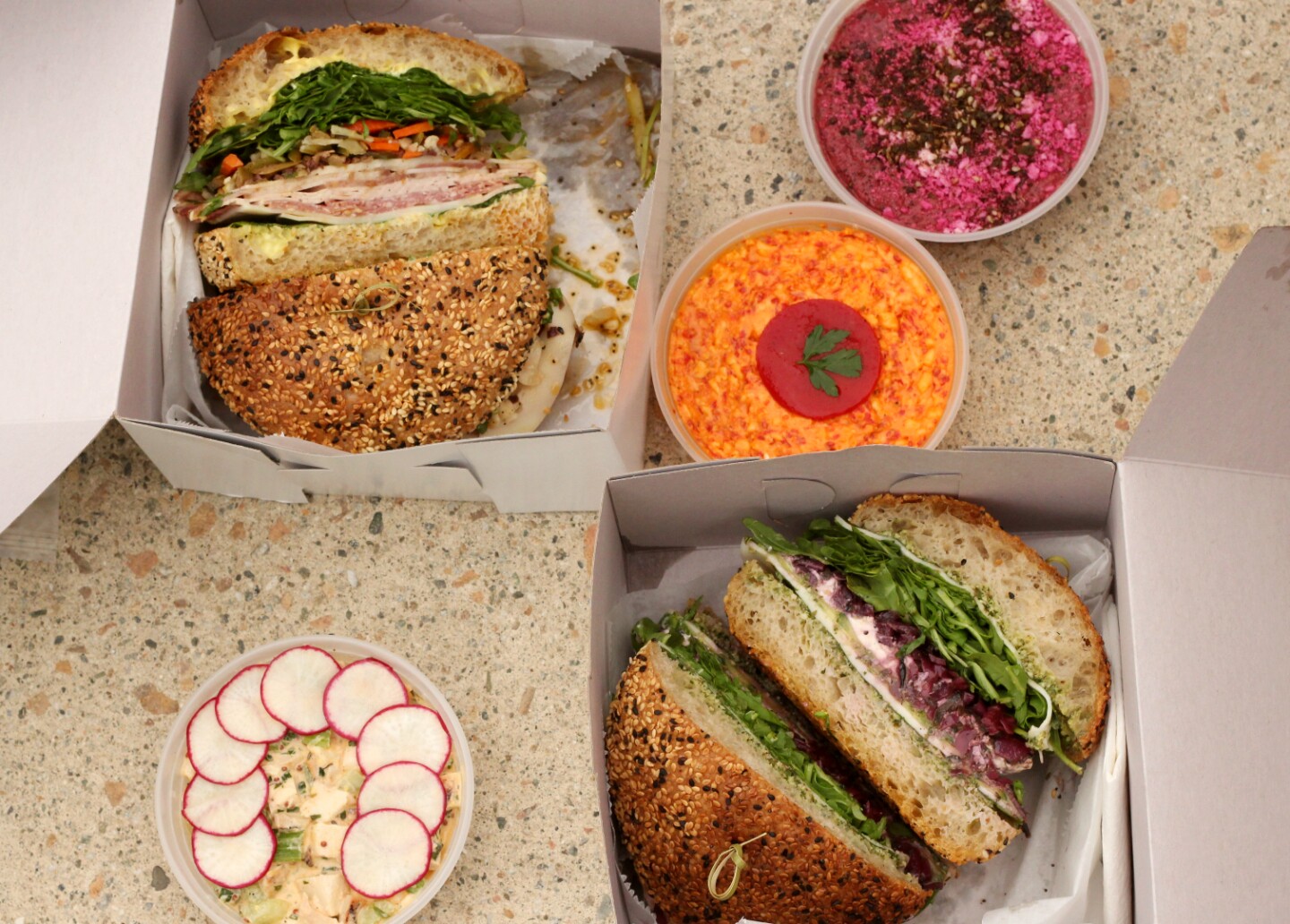 an overhead shot of two sandwiches in cardboard boxes and three small containers of dips