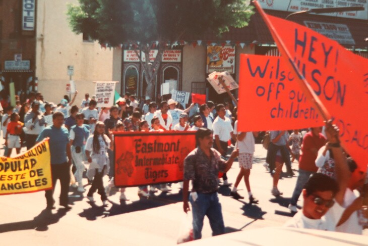 Protester carry red signs that protest then-Gov. Pete Wilson