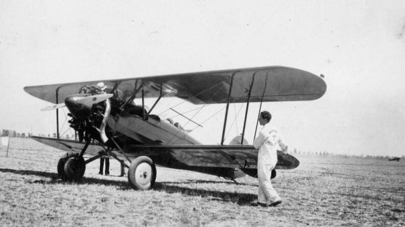An old black and white photo of a planes sitting in a barren field. There's a person standing next to it.