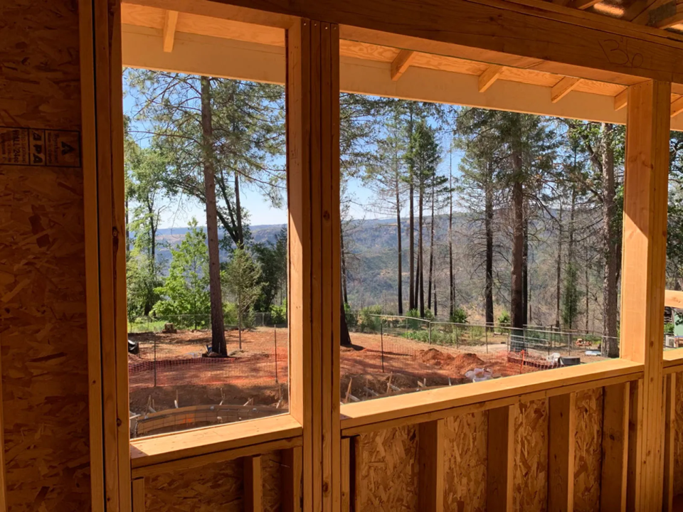 Trees are in the foreground and a ridgeline is in the background of a view scene through the wooden frame of a home under construction