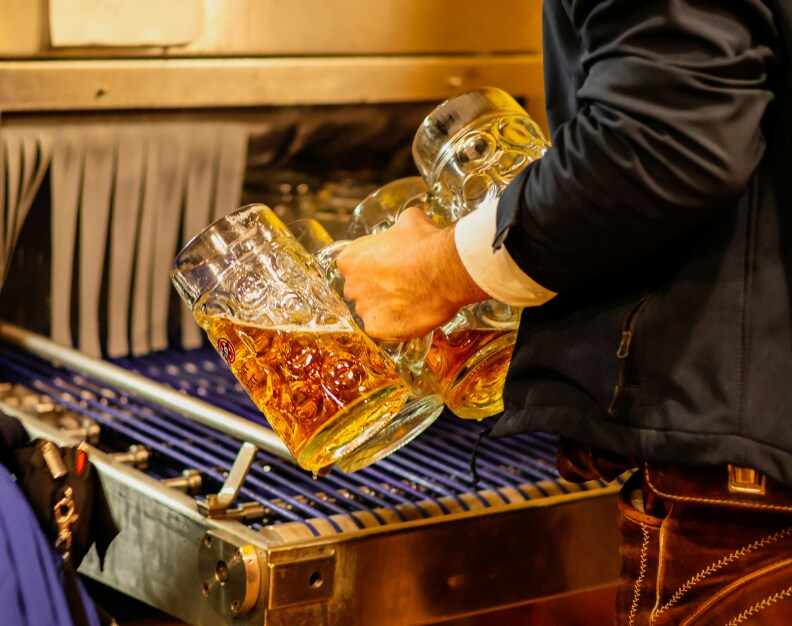A person holding tall mugs of beer over a machine with purple lining.
