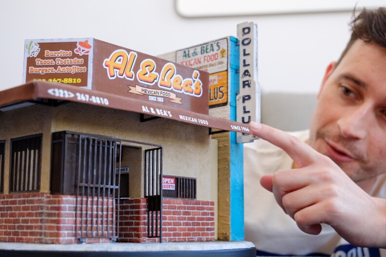 A close-up of the Al & Bea's miniature building. A man is behind it touching the small building with his index finger.