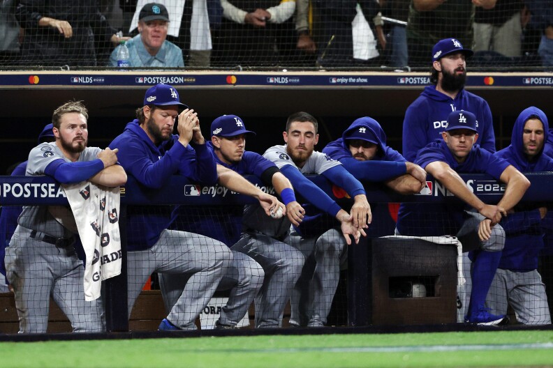 Baseball players in Dodgers blue lean over the dugout and look dejected.