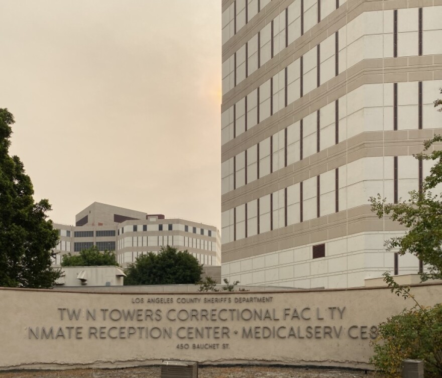 A sign outside a building reads "Twin Towers Correctional Facility Inmate Reception Center." A tower rises in the distance.