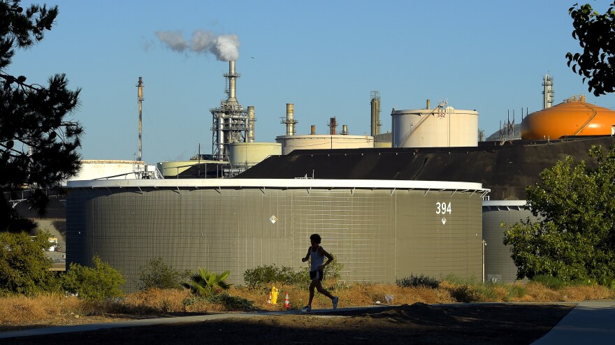 A large reservoir tank with refinery machinery in the background.