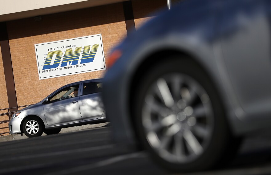 Cars are parked outside a brick building with a sign reading: State of California DMV