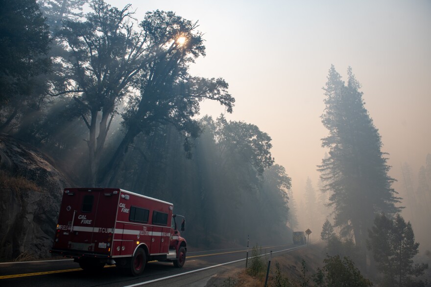A red fire truck drives down a smoky mountain road.