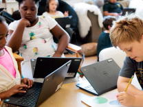 Children write and use laptops in a classroom.