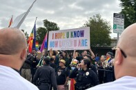 A group of LGBTQ+ supporters stand behind a police line outside the school holding up the sign I hope you know how loved you are in rainbow and trans pride flag colors.