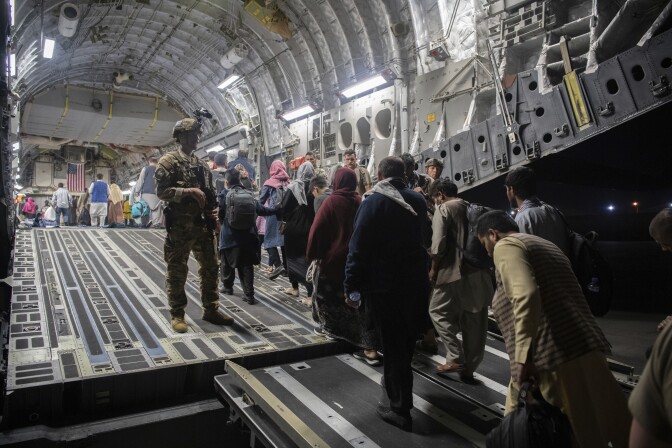 People board a cargo plane from the back.