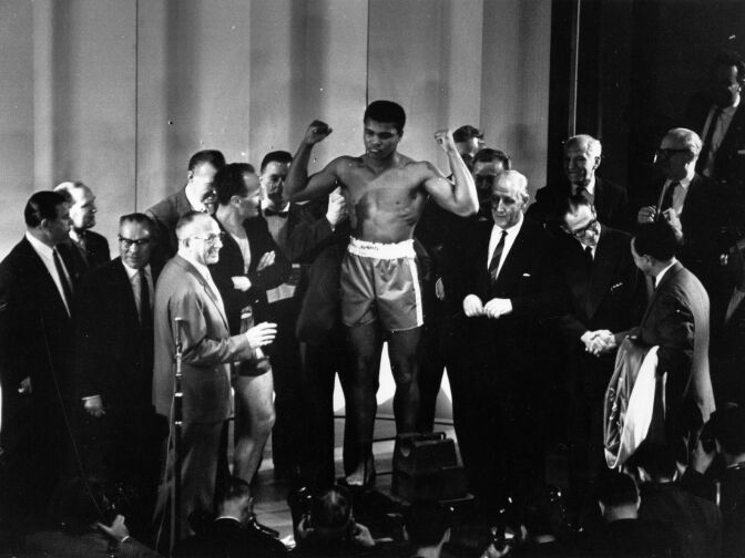 1963: American boxer Cassius Clay weighs in before his world heavyweight title fight against British boxer Henry Cooper.