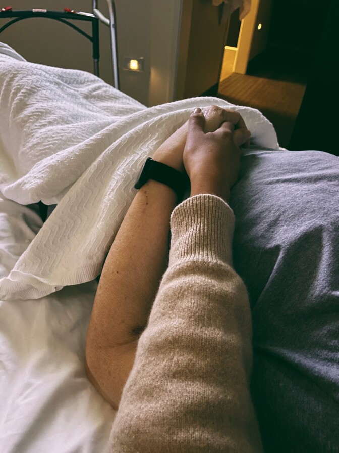 Two people hold hands, as one rests in a bed.