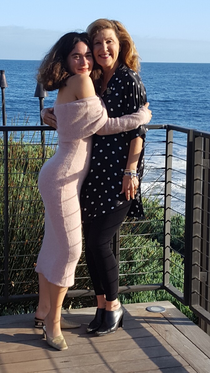A mother and daughter pose on a balcony in front of the sea
