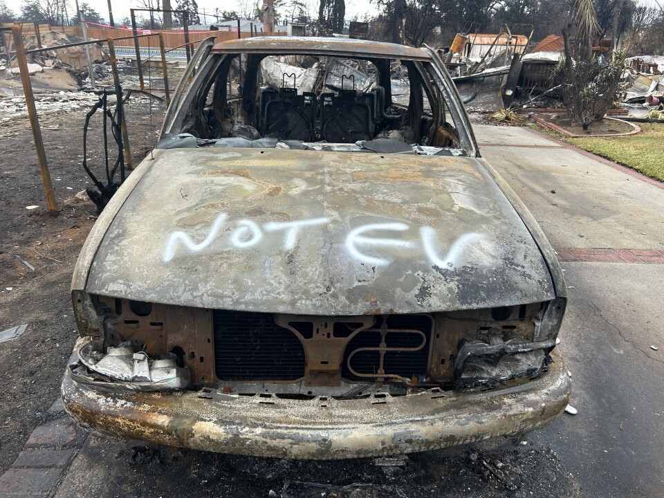 A burned out husk of a car with white spray paint on the hood reading "NOT EV"