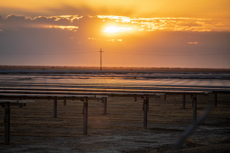 Rows of solar panels are shown outside as the sun peeks behind clouds on the horizon.