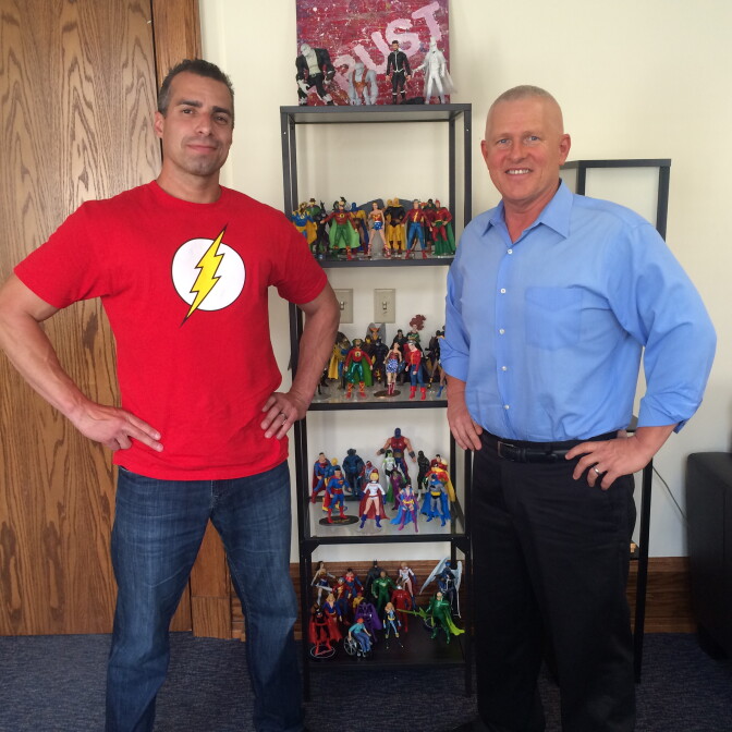 A Martinez (l) and LA City Councilman Mike Bonin pose in front of just one half of Bonin's collection of superhero action figures at his City Hall office. He apparently has even more at home.