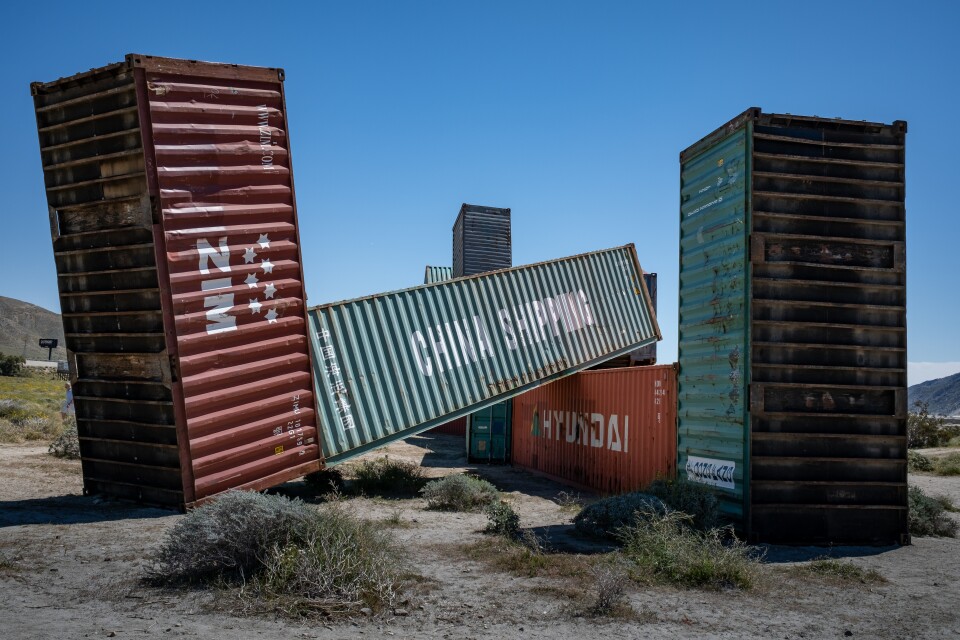rusted massive shipping containers lie horizontal and vertical against a blue sky