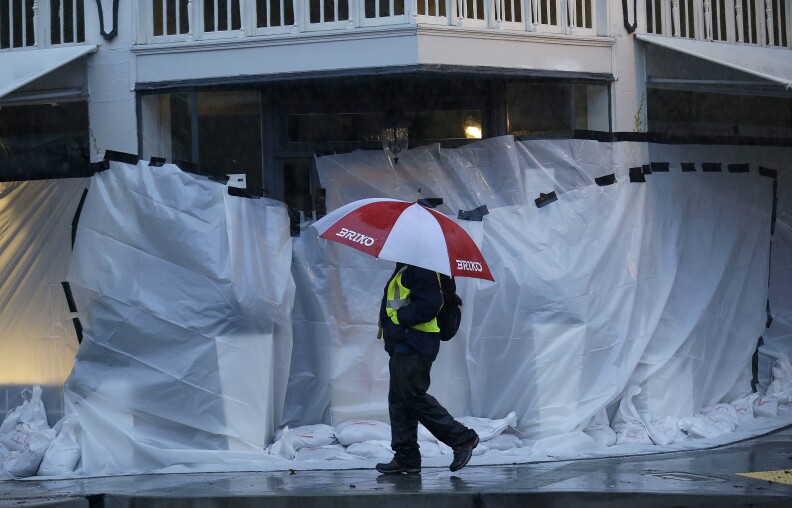 A man walks in the rain past a covered storefront in San Anselmo, Calif., on Jan. 7, 2017. On the California coast, weather forecasters anticipated a storm surge from the Pacific called an atmospheric river to dump several inches of rain from Sonoma to Monterey counties, and up to a foot in isolated places in the Santa Cruz mountains. 