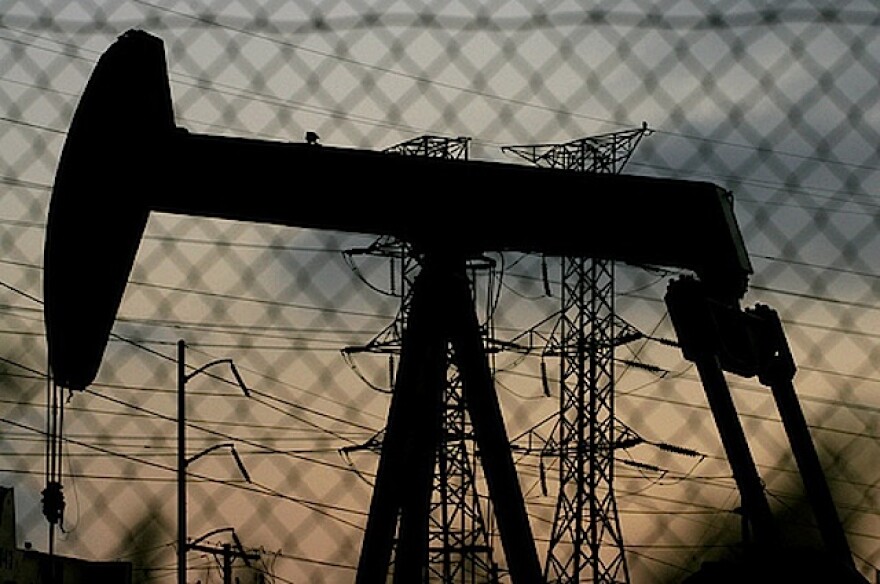 Oil drill seen through chainlink fence in Baldwin Hills at dusk.