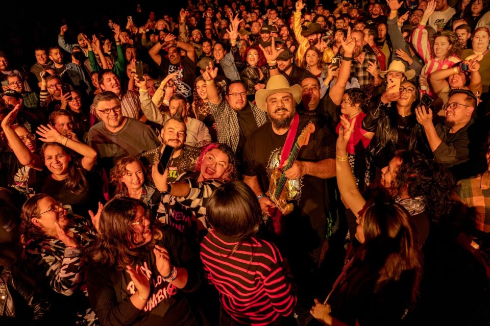 A crowd of people stand around a guitarist and cheer as he performs.