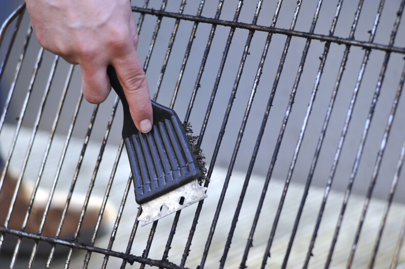 A hand is cleaning the grill with scrubber.