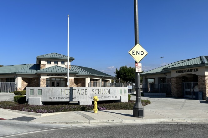 A wide shot of a school with a large concrete sign in front reading Heritage School. To the right, there's a building with a green roof labeled Kindergarten. To the left is a building with a green roof labled Administration. 