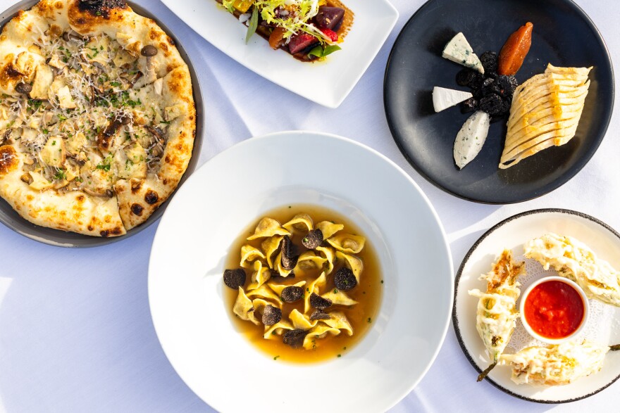 A photo taken from above of various white plates full of pizza, pasta, fried vegetables, and a cheese plate.