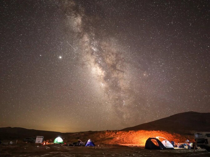 Bright objects in the night sky appear in a very starry sky over a campsite. 