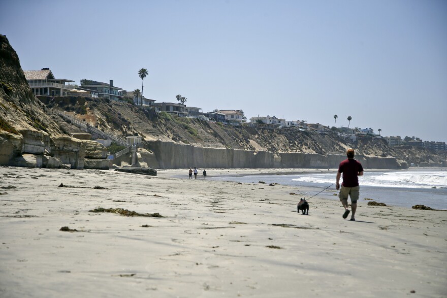 File: Beach goers walk the sand in Solana Beach, Calif., below homes precariously perched atop cliffs of which some are supported by sea walls meant to hold back the ocean Monday, May 20, 2013.