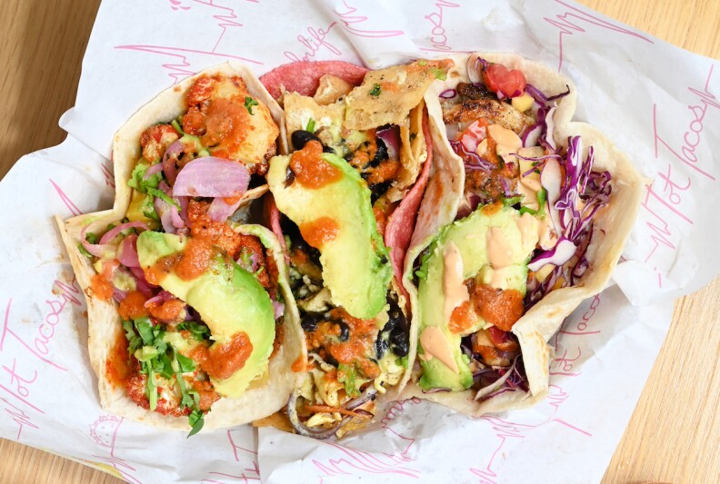 looking down on three tacos topped with avocado and salsa sitting on white paper