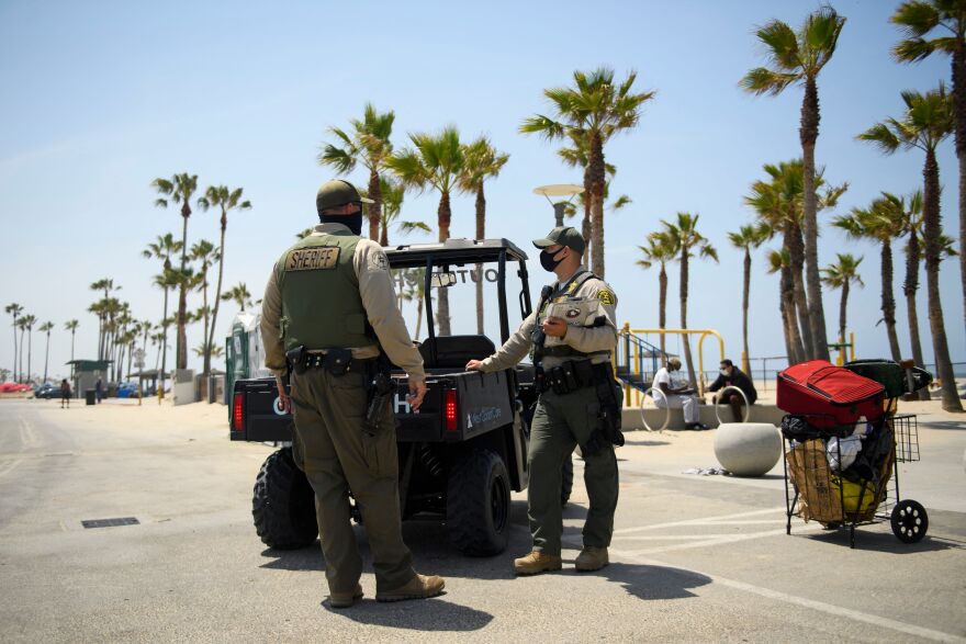 L.A. County Sheriff's deputies stand next to a small jeep vehicle at the Venice Beach Boardwalk.