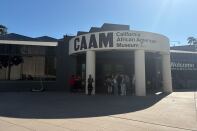People gather in the shade under the sign for CAAM, the California African American Museum.