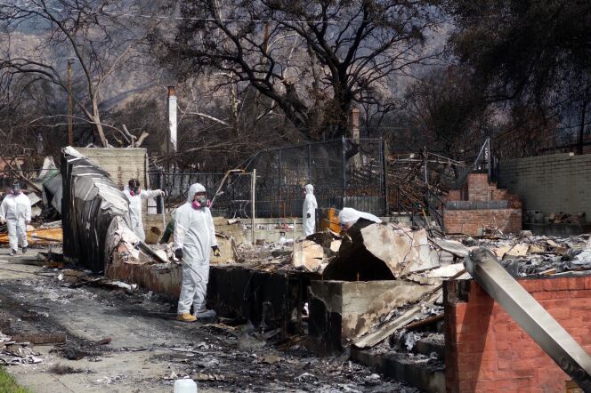 Workers in white suits covering their entire body and face masks remove debris from a burnt home.